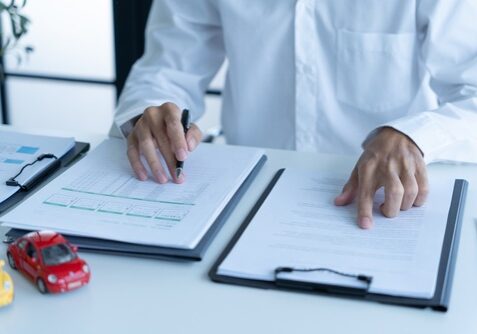 person reviewing car insurance documents on desk with toy car models